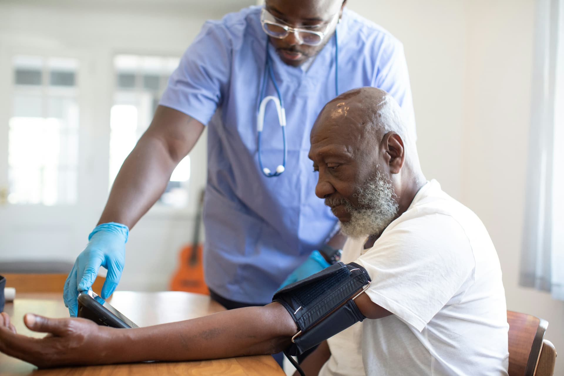 A nurse taking an older man's blood pressure at his kitchen table